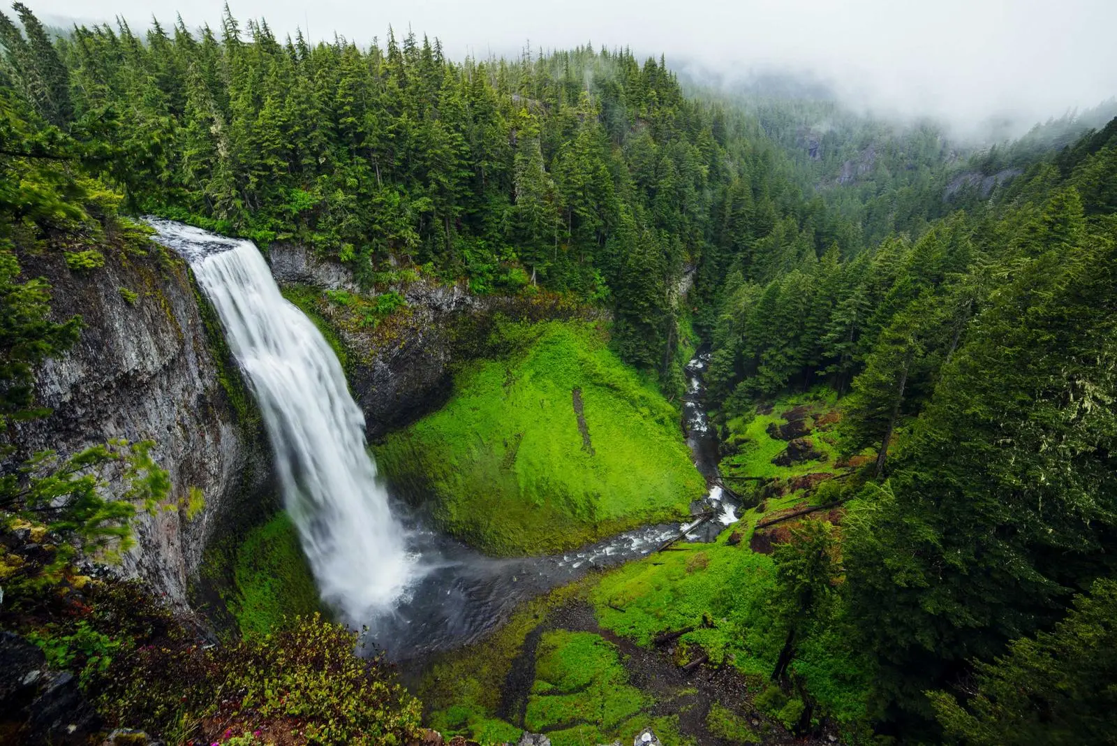 A waterfall flowing into a green, misty valley